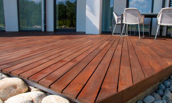 Freshly stained wooden deck with clean lines and an outdoor dining setup, demonstrating proper maintenance and repair techniques.