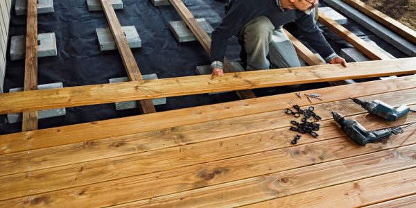 A homeowner installing a wooden deck with tools and fasteners, ensuring a smooth and secure deck installation.