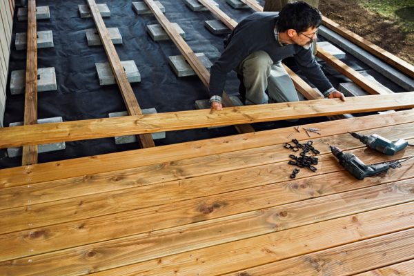 A homeowner installing a wooden deck with tools and fasteners, ensuring a smooth and secure deck installation.